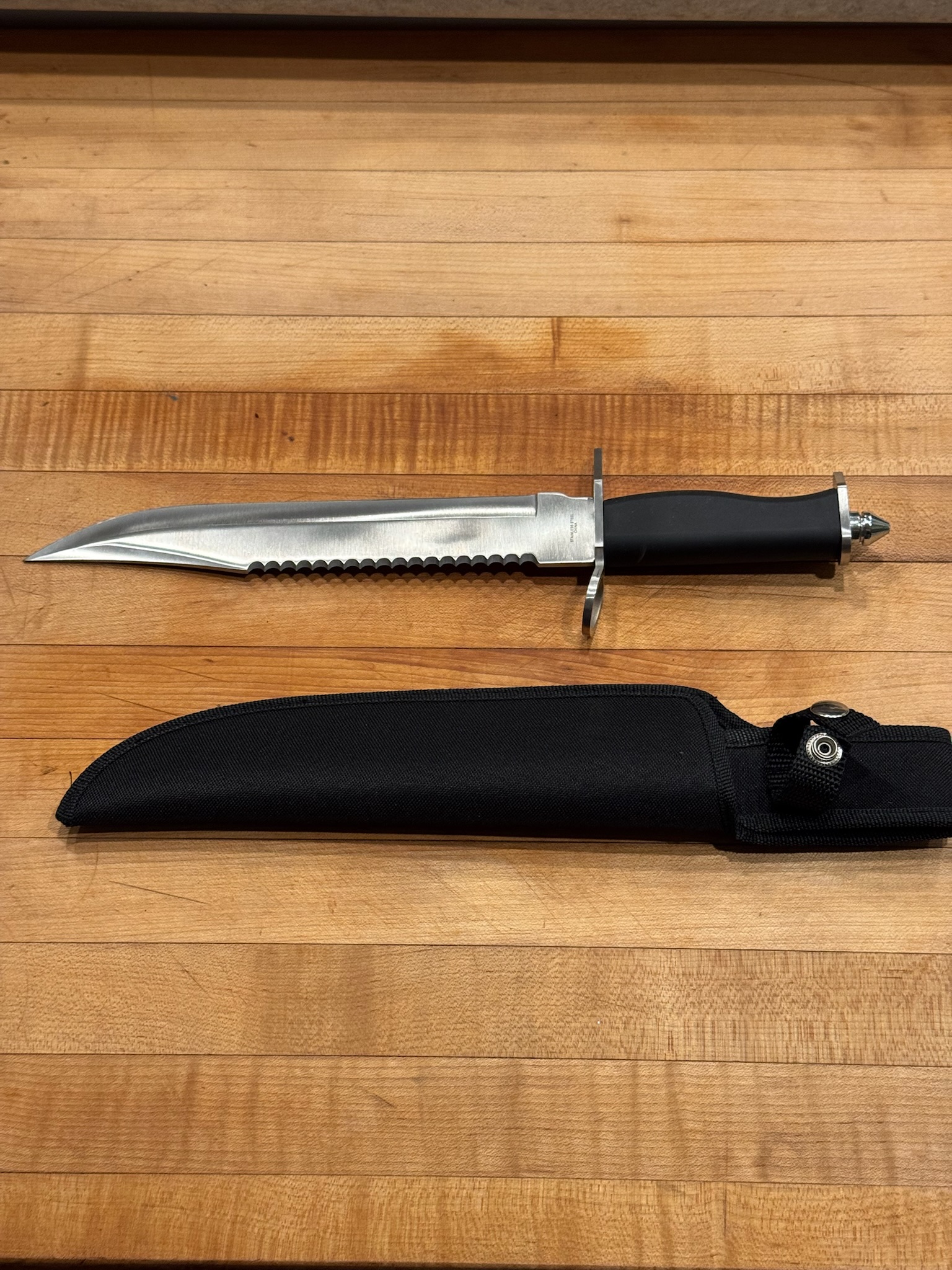 A long serrated blade and sheath on a wood surface