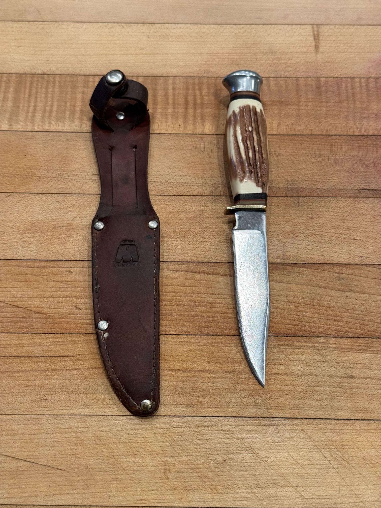 A vintage-style knife with a light handle beside its sheath